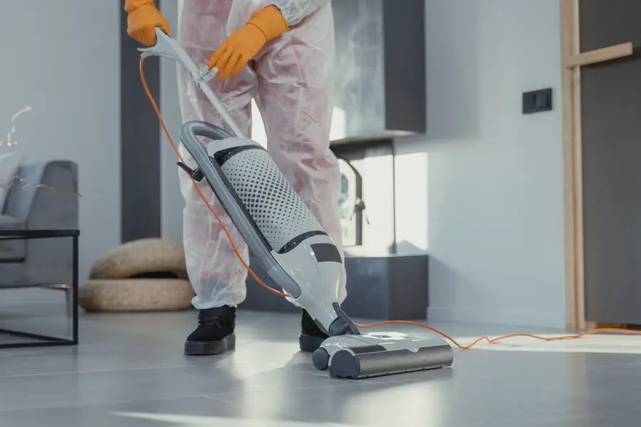 A technician in a white suit using an upright vacuum in a bright room.